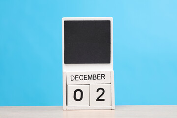 White wooden block monthly calendar with the date december 2 on the table, blue background. Planning, deadline