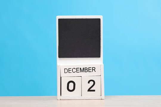 White wooden block monthly calendar with the date december 2 on the table, blue background. Planning, deadline