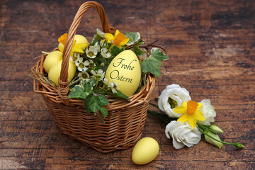 Grußkarte Frohe Ostern. Dekorativer Osterkorb mit Blumen und einem beschrifteten Osterei mit dem...