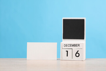 White wooden block monthly calendar with the date december 16 and white business card on the table, blue background. Planning, deadline