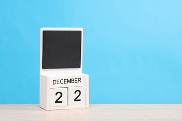White wooden block monthly calendar with the date december 22 on the table, blue background. Planning, deadline