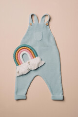Pastel color knitted romper, rainbow toy on beige background. Set of baby stuff and accessories for newborn. Baby shower or baby care concept. Fashion newborn. Flat lay, top view