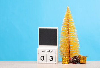 Merry Christmas and happy new year. White block calendar with date january 03 and Christmas decor on table, blue background