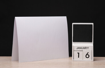 White wooden block monthly calendar with the date january 16 and table flyer mockup on the table, black blackbackground. Planning