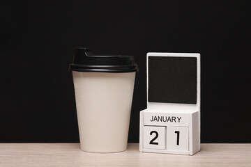 White wooden block monthly calendar with the date january 21 and coffee cup on the table, black blackbackground. Planning