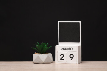 White wooden block monthly calendar with the date january 29 and decorative plant on the table, black blackbackground. Planning