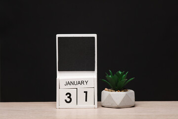 White wooden block monthly calendar with the date january 31 and decorative plant on the table,...