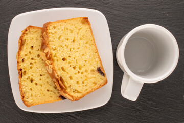 Two pieces of sweet homemade raisin cake with white saucer and cup on slate stone, macro, top view.