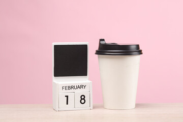 White wooden block monthly calendar with the date february 18 and coffee cup on the table, pink...