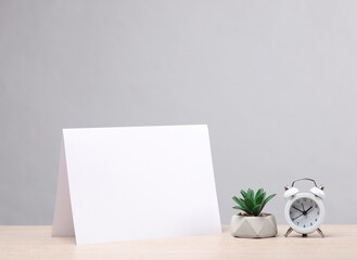 Blank white paper calendar or table flyer mockup with alarm clock, plant on gray background