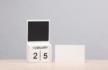White wooden block monthly calendar with the date february 25 and white business card on the table, gray background. Planning, business concept
