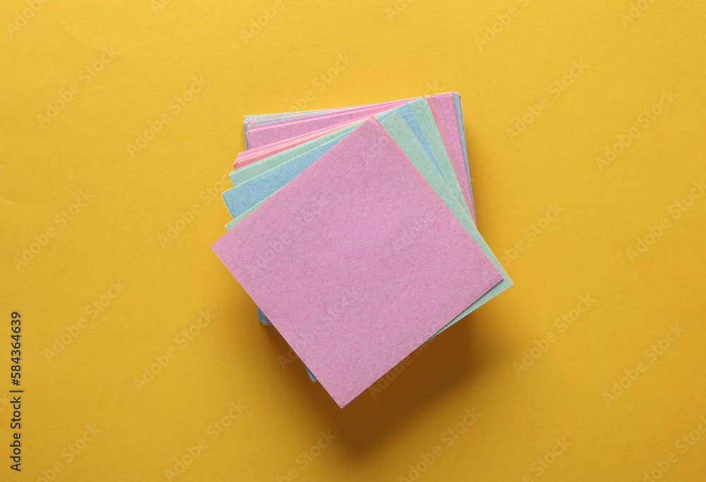 Poster stack of colored square memo sheets of papers on yellow background. top view