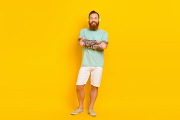 Fototapeta na wymiar Full length photo of young redhair man wear green t-shirt folded arms tattoo brutal listen jazz music earphones isolated on yellow color background