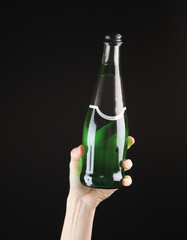 Female hand holding a bottle of green Irish beer on black background.