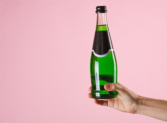 Female hand holding bottle of green Irish beer on pink background