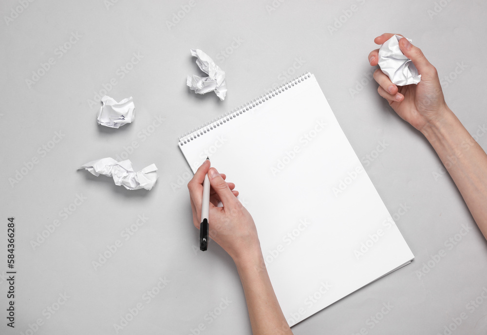 Poster lack of idea. female hands are bishut in a sketchbook and crumpling sheets of paper on a gray backgr