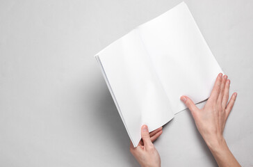 Female hands leaf through a magazine or catalog with blank white pages on a gray background....