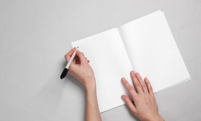 Women's hands write with a pen in a notebook on a gray background. White blank mockup. Template for design