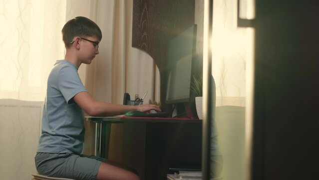 Boy writes program code at home using computer.Authentic Action,Home Window,Sun Flare,Bright Light