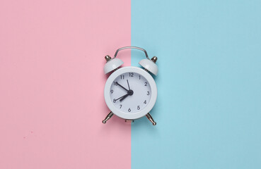 White miniature alarm clock on a pink blue background. Top view