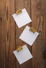 White empty square memo pieces of paper with binders on wooden table. Template for design.