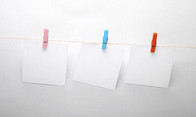 White empty square memo pieces of paper with clothespins on gray background. Template for design.