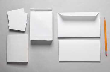 Mockup with white paper office objects. White empty envelope with a letter, lunch bag, business card, notepad and memo papers on a gray background. Template for design. Top view