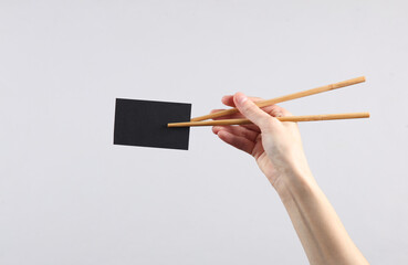 Chinese chopsticks with black business card in a female hand on a gray background
