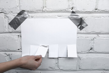 Woman's hand tears off stripes ad with phone number on brick wall background. Template for design.