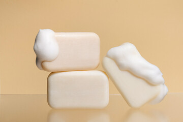 Pieces of light natural soap with foam stand on glass on a beige plain background. Concept of cosmetic products for skin care, beauty and spa.