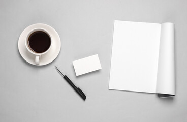 Obraz na płótnie Canvas Creative template for design. Mockup of an open magazine with white pages, empty business card, pen and coffee cup on gray background. Top view