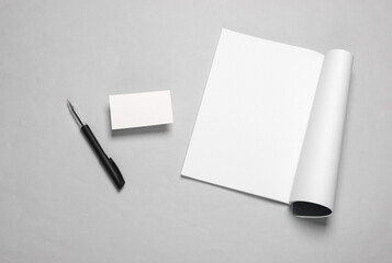 Creative template for design. Mockup of an open magazine with white pages, empty business card, pen on gray background. Top view