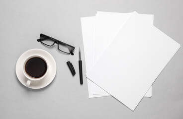 White blank sheets of a4 paper size or documents mockup with pen, eyeglasses and coffee cup on a gray background. Template for design. Top view. Copy space