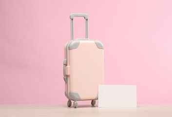 Travel luggage miniature with a blank business card on a pink background. Travel, trip, vacation concept. Tour firm corporate identity. Template for design