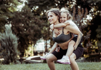 Athletic mom squatting with her little daughter outdoors, healthy lifestyle, fitness active family...