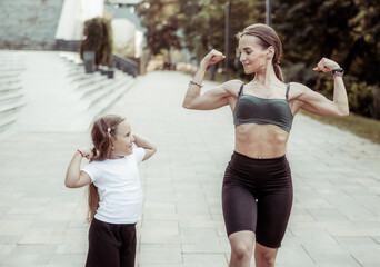 Strong mom and little daughter posing outdoors showing their muscles