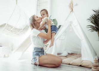 Maternal love concept. Mom hugs and kisses her little daughter on the cheek in room with wigwam © splitov27