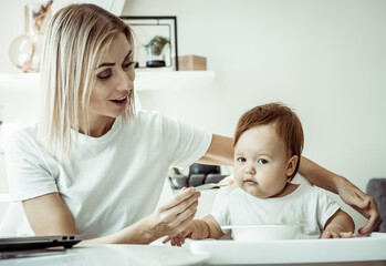 A caring mother feeds her baby from a spoon while sitting at a table