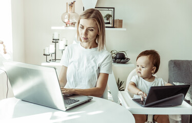 Mom and her little daughter use laptops and sit at the tables at home. Maternity, work and maternity