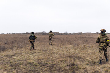 Group of armed Ukrainian soldiers walks through steppe.