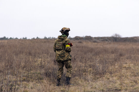 Rear view of armed Ukrainian soldier walking in steppe in uniform and helmet.