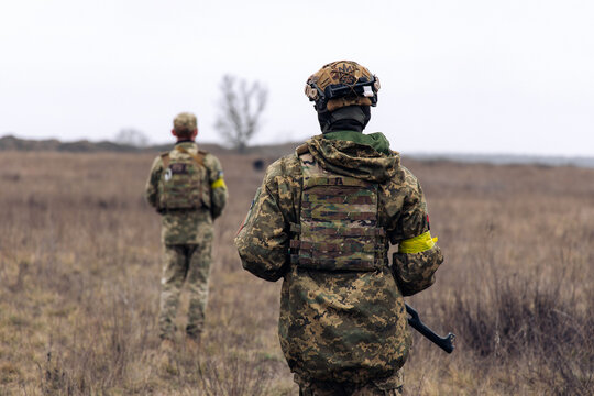 Rear view of two armed Ukrainian soldiers walking in steppe in uniform and helmets.
