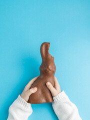 Chocolate Easter bunny with ears bitten off in hands of child on blue background, family concept. Vertical, top view, copy space