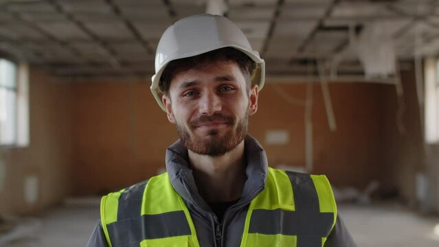 The construction engineer turns to the camera and smiling. Front view of cheerful construction worker in hardhat and reflective vest