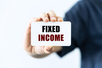Fixed income text on blank business card being held by a woman's hand with blurred background. Business concept about fixed income.