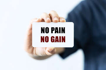 No pain no gain text on blank business card being held by a woman's hand with blurred background. Business concept about training hard.