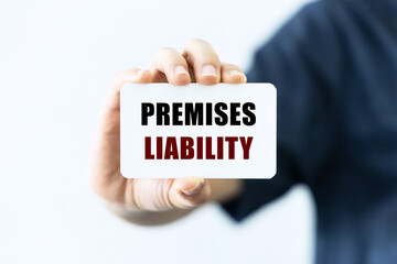 Premises liability text on blank business card being held by a woman's hand with blurred...