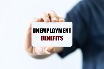 Unemployment benefits text on blank business card being held by a woman's hand with blurred background. Business concept about unemployment benefits.