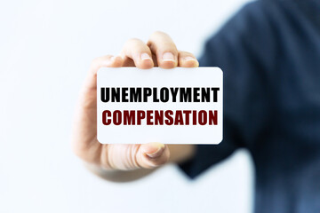 Unemployment compensation text on blank business card being held by a woman's hand with blurred background. Business concept about unemployment compensation.
