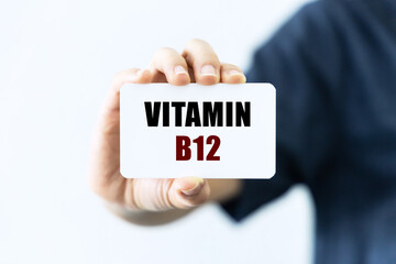 Vitamin B12 text on blank business card being held by a woman's hand with blurred background. Business concept about vitamin.